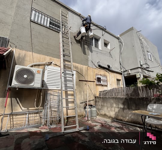 אדם עובד בגובה על קיר חיצוני עם סולם